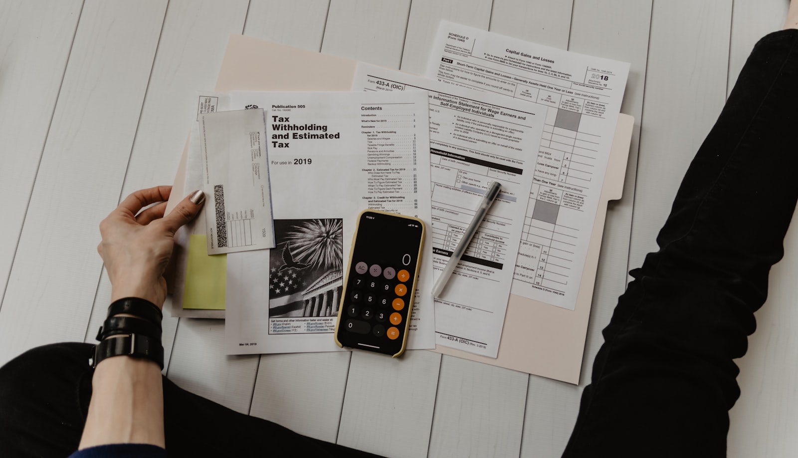 A calculator, paperwork, and laptop on a desk, representing pricing, material costs, and product profitability review.