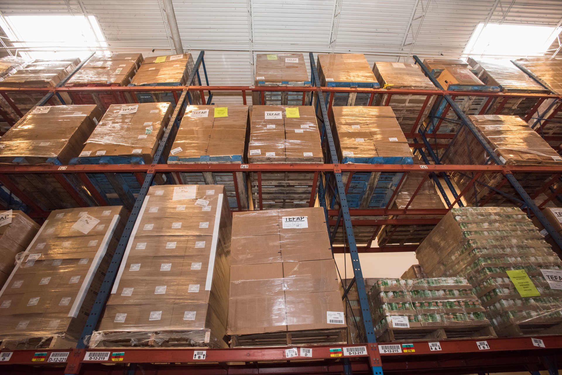 Pallets of labeled cartons stored on tall warehouse racks beneath a high industrial ceiling.