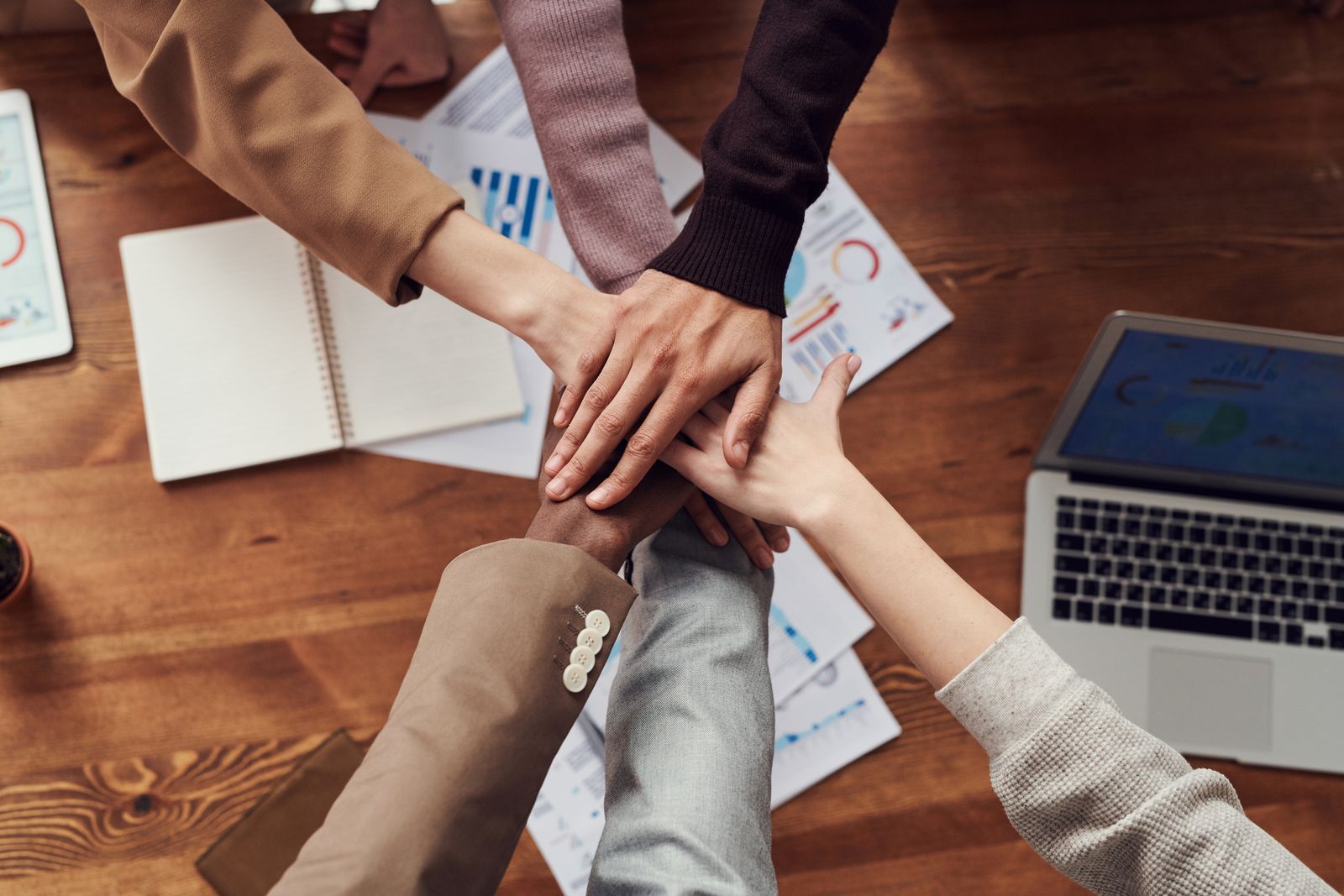 Several people gathered around a wooden table with their hands stacked together in a collaborative gesture.